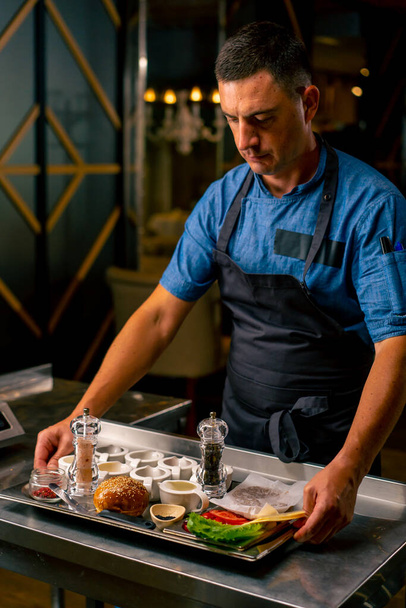 Yemek hazırlarken profesyonel bir İtalyan restoranının mutfağında duran üniformalı şefin portresi. - Fotoğraf, Görsel