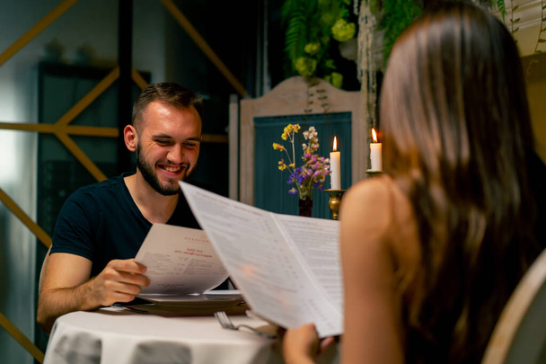 Jovem casal cara e menina sentado em um restaurante italiano olhando para o menu e escolher o que pedir para o jantar enquanto na data - Foto, Imagem