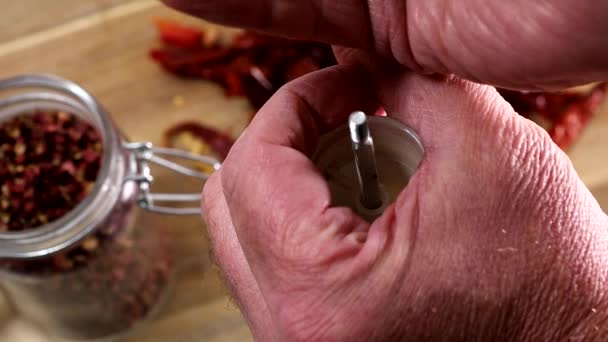 Een hand vult een pepermolen met gedroogde peper in een keuken over een houten plank.  - Video