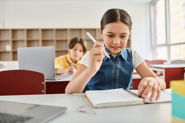 Mladá dívka sedí za stolem, drží pero a zápisník, plně zapojena do psaní nebo kreslení. - Fotografie, Obrázek