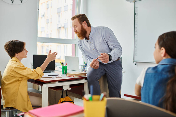 Un homme se tient devant un bureau, enseignant passionnément un jeune enfant dans un cadre de classe dynamique. - Photo, image