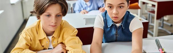 Um menino e uma menina estão sentados em uma mesa em uma sala de aula brilhante e animada - Foto, Imagem
