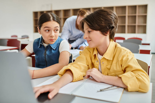 Ένα αγόρι και ένα κορίτσι ασχολούνται με προσοχή σε ένα τραπέζι με ένα φορητό υπολογιστή, απορροφάται σε μια κοινή μαθησιακή εμπειρία - Φωτογραφία, εικόνα