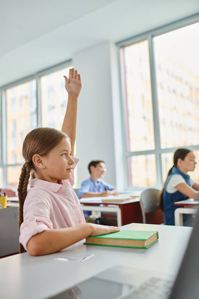 Молода дівчина з довгим волоссям піднімає руку в барвистому, жвавому класі. - Фото, зображення