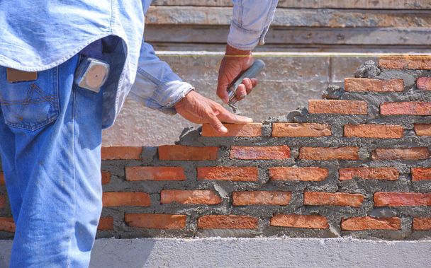 Nahaufnahme von Bauarbeiterhänden macht niedrige Mauer aus Ziegelstein in Hausbaustelle - Foto, Bild