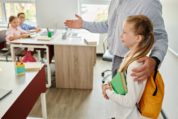 Un homme, un enseignant, se tient à côté d'une petite fille dans un cadre de bureau animé, offrant conseils et soutien. - Photo, image
