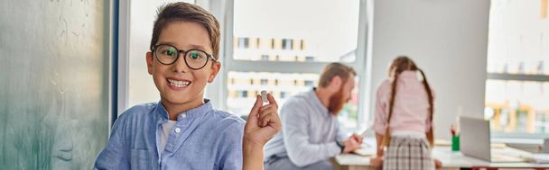 Un garçon se tient en confiance devant un mur, lunettes ajoutant une touche intelligente à son comportement. - Photo, image