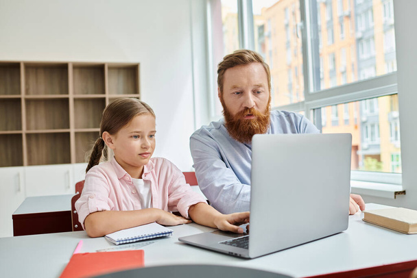 Een man en een klein meisje zitten voor een laptop, verdiept in een leeractiviteit. De man lijkt het meisje te onderwijzen en te leiden terwijl ze aandachtig luistert.. - Foto, afbeelding