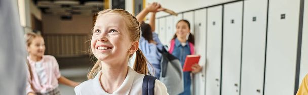 Разнообразная группа молодых девушек, стоящих возле шкафчиков в динамичном школьном коридоре, в то время как учитель-мужчина инструктирует их. - Фото, изображение