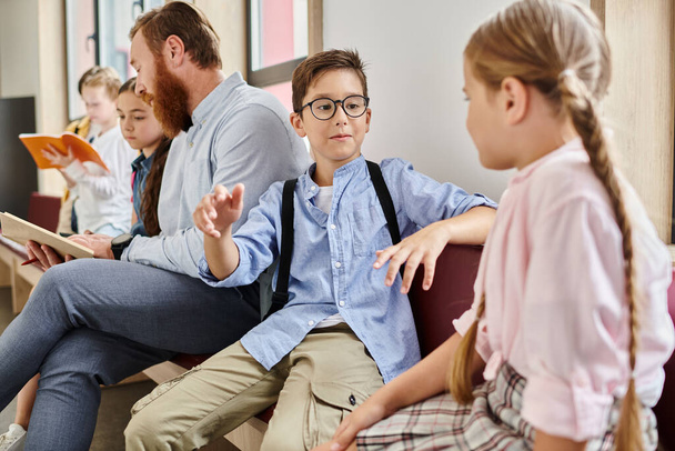 Un maestro masculino instruye a un grupo de niños diversos en un ambiente brillante y animado en el aula, sentados uno al lado del otro y absortos en el aprendizaje. - Foto, imagen