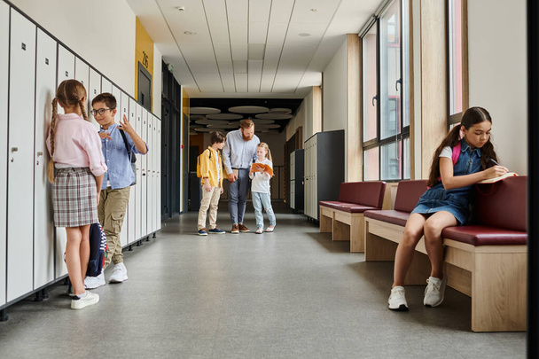 gyerekek egy csoportja áll a folyosón a szekrények mellett, miközben egy tanár tanítja őket fényes, élénk osztálytermi környezetben. - Fotó, kép