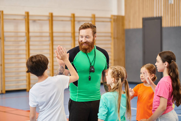 Un hombre barbudo está de pie con confianza frente a un grupo de niños, involucrándolos en un ambiente animado en el aula. - Foto, imagen