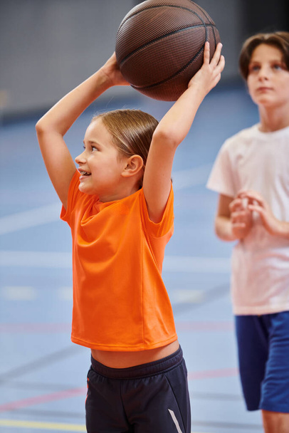 Młoda dziewczyna z radością trzyma wysoko w powietrzu koszykówkę, promieniując poczuciem ekscytacji i pasji do gry. - Zdjęcie, obraz