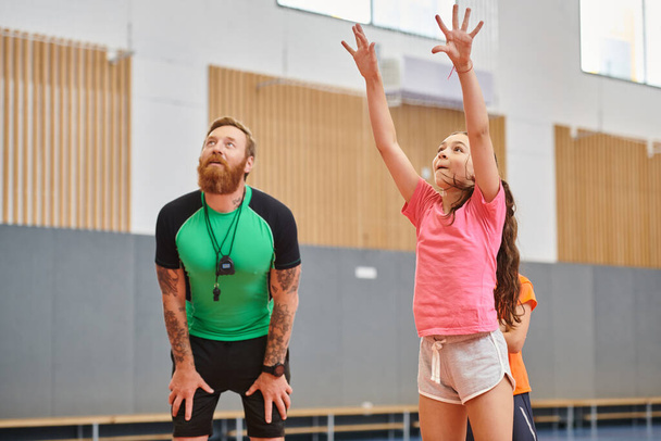 Ένας άνδρας και μια νεαρή κοπέλα παίζουν δυναμικά μπάσκετ σε ένα γυμναστήριο, επιδεικνύοντας ομαδικότητα, επιδεξιότητα και συντροφικότητα.. - Φωτογραφία, εικόνα