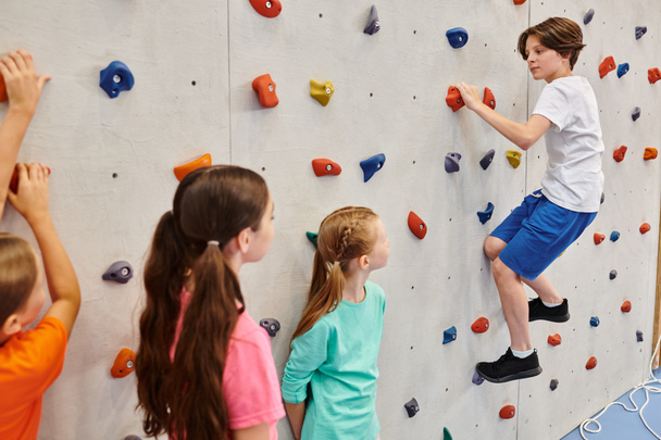 Un gruppo di bambini si riunisce davanti a una parete di arrampicata, ascoltando attentamente le istruzioni dei loro insegnanti prima di tentare di scalare la parete.. - Foto, immagini