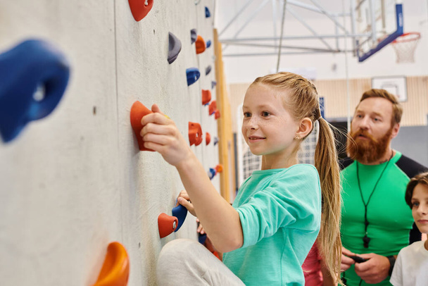 leraar en kinderen, verzameld rond een kleurrijke klimwand, bezig met klimmen en het ontvangen van instructies - Foto, afbeelding