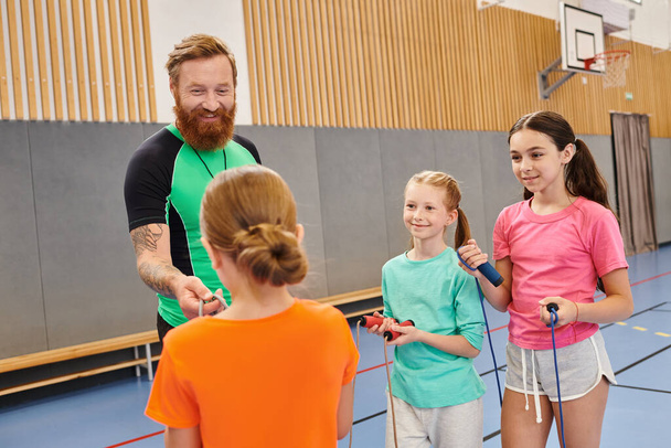 Divers groupes de personnes, y compris des enfants et un enseignant, debout attentivement les uns autour des autres dans une salle de gym animée, l'enseignant instruisant avec enthousiasme. - Photo, image