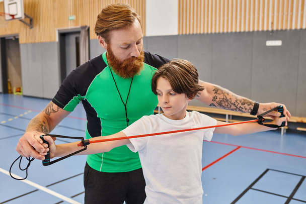 Ein Mann unterrichtet einen Jungen in einem lebhaften Fitnessstudio - Foto, Bild