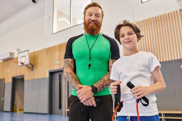 Un hombre está junto a un niño en un gimnasio, practicando actividades físicas y entrenando juntos.. - Foto, imagen