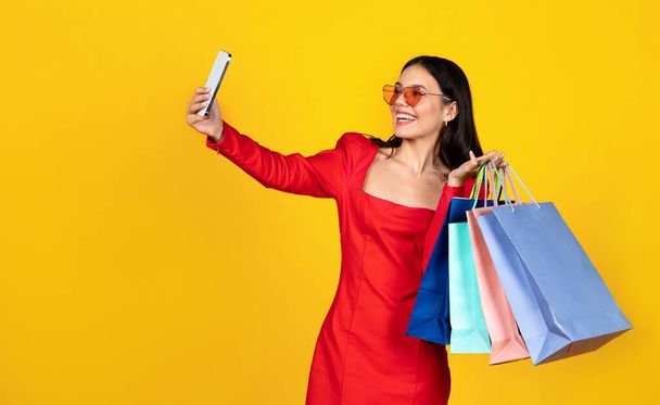 Boldog fiatal nő bevásárló táskák fotózás Selfie Smartphone, mosolygó nő Stílusos szemüveg hordozó vásárlások és pózol a mobiltelefon kamera, élvezi a szezonális értékesítés, másolás tér - Fotó, kép
