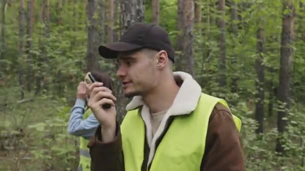 Tiro de seguimiento de rescatador profesional masculino caucásico en chaleco de ácido verde caminando en el bosque y hablando en la radio - Metraje, vídeo