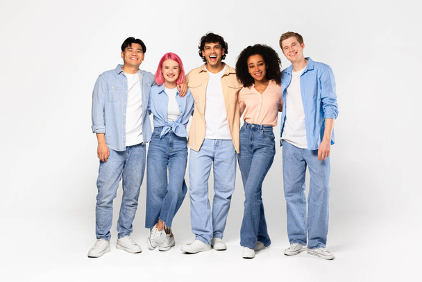 Happy young multiracial students posing, hugging, looking and smiling at camera, posing isolated on white studio background, copy space, full length. Study abroad, modern study and teamwork. - Foto, imagen
