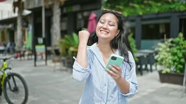 Νεαρή Κινέζα γυναίκα που χρησιμοποιεί smartphone γιορτάζει στη βεράντα της καφετέριας - Πλάνα, βίντεο