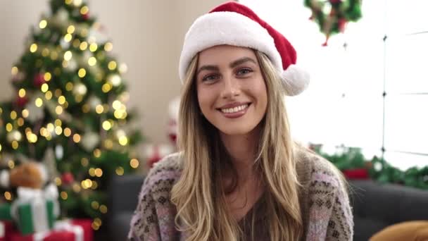 Joven rubia de pie junto al árbol de navidad besándose en casa - Metraje, vídeo