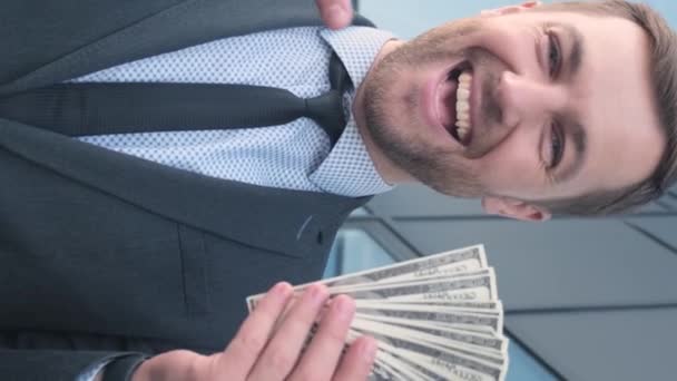 Gelukkige zakenman toont verdiend geld. Een gelukkig man heeft dollars in zijn handen. Bedrijfs- en financieel concept. Verticale video - Video