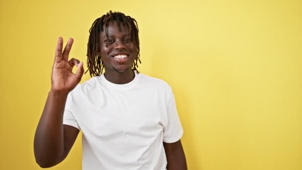 Afro-Amerikaanse man doet ok gebaar glimlachen over geïsoleerde gele achtergrond - Video