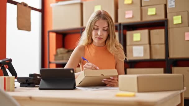 Mujer rubia joven comercio electrónico trabajador de negocios utilizando touchpad escritura en el paquete en la oficina - Imágenes, Vídeo