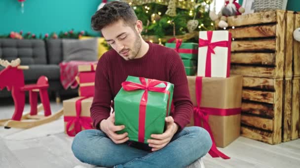 Fiatal spanyol férfi kezében karácsonyi ajándék mosolyog otthon - Felvétel, videó