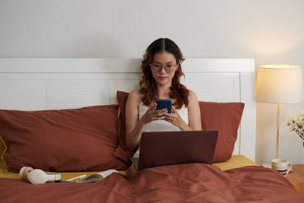 Mladá žena sedí v posteli s notebookem a textové spolupracovníky - Fotografie, Obrázek