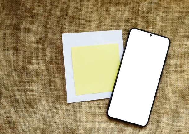 Teléfono móvil con pantalla vacía maqueta en una arpillera beige neutra, plantilla de marca comercial minimalista, espacio de copia en hoja de papel - Foto, imagen