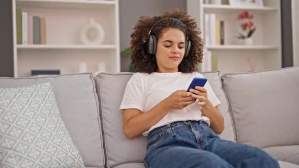Νεαρή όμορφη ισπανόφωνη γυναίκα ακούγοντας μουσική χαλαρή στον καναπέ στο σπίτι - Πλάνα, βίντεο