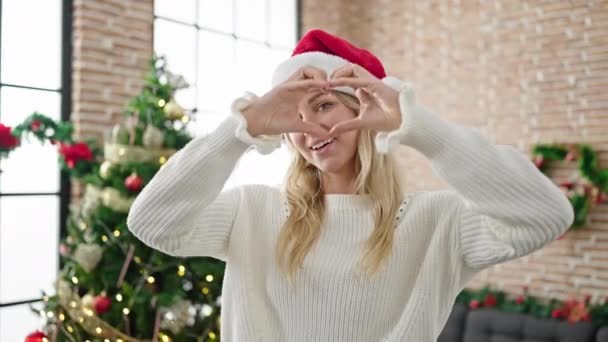 Fiatal szőke nő ünnepli karácsony csinál szív alakja a kezét otthon - Felvétel, videó