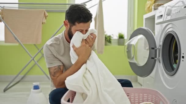 Молодий іспаномовний чоловік миє одяг, пахне чистим рушником у пральні - Кадри, відео
