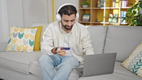 Nuori latinomies ostokset kannettava tietokone ja luottokortti istuu sohvalla kotona - Materiaali, video