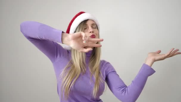 Mujer rubia joven con sombrero de Navidad bailando sobre fondo blanco aislado - Imágenes, Vídeo