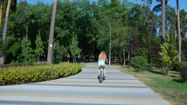 Blondes Mädchen läuft auf einem Mountainbike in einem Stadtpark. Ein Mädchen fährt auf einem Fahrrad mit breiten Reifen und Lauffläche durch ein grünes Blumenbeet. Hochwertiges 4k Filmmaterial - Filmmaterial, Video