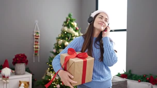 Молодая кавказская женщина празднует Рождество, слушая музыку и танцуя дома - Кадры, видео
