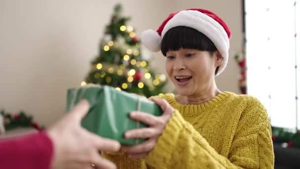 Νεαρή Κινέζα γυναίκα κρατώντας δώρο στέκεται δίπλα στο χριστουγεννιάτικο δέντρο στο σπίτι - Πλάνα, βίντεο