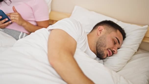Hombre y mujer pareja usando smartphone mientras su novio duerme en el dormitorio - Metraje, vídeo