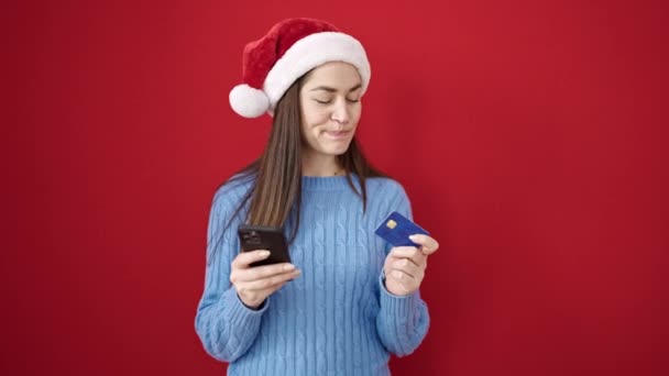 Nuori valkoihoinen nainen tekee joulua verkkokaupoissa älypuhelimella eristetyllä punaisella taustalla - Materiaali, video