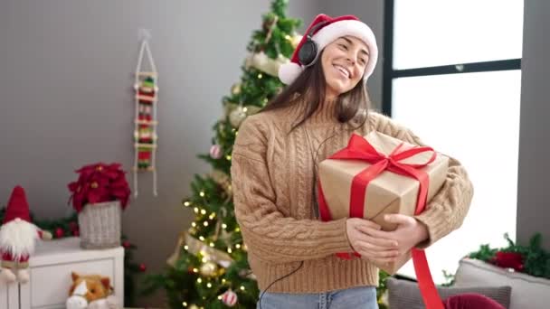 Νεαρή όμορφη Ισπανίδα που κρατάει χριστουγεννιάτικο δώρο ακούγοντας μουσική και χορεύοντας στο σπίτι - Πλάνα, βίντεο