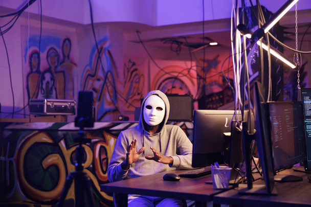 Hacker in anonymer Maske streamen illegale Online-Aktivitäten auf dem Smartphone ins Darkweb. Kriminelle Aufzeichnungsdrohungen auf dem Handy und Verletzung von Privatsphäre-Daten im Versteck - Foto, Bild