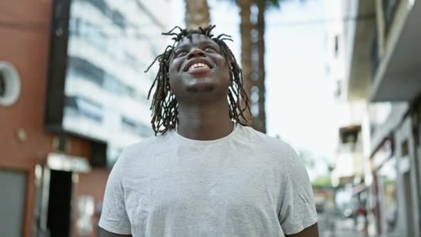 Hombre afroamericano sonriendo confiado mirando al cielo celebrando en la calle - Imágenes, Vídeo