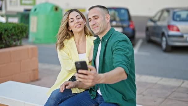 Мужчина и женщина делают селфи на смартфоне, сидя на скамейке в парке - Кадры, видео
