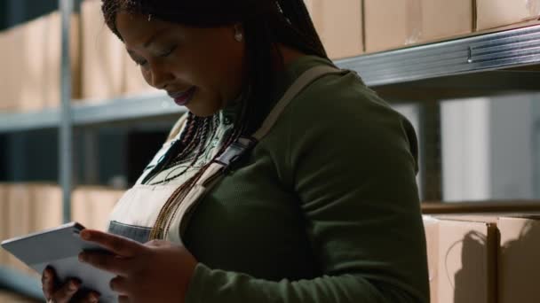 Közelkép afro-amerikai raktár logisztikai igazgató holding tabletta, ellenőrzése csomagolt kartondobozok csomagok, biztosítva az optimális műveletek professzionális raktár - Felvétel, videó