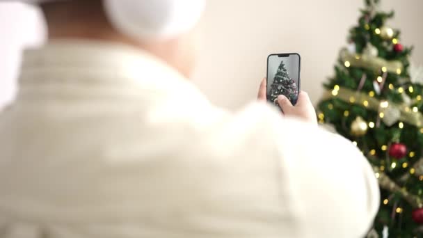 Νεαρός ισπανόφωνος άνδρας ηχογράφηση βίντεο από smartphone με χριστουγεννιάτικη διακόσμηση στο σπίτι - Πλάνα, βίντεο